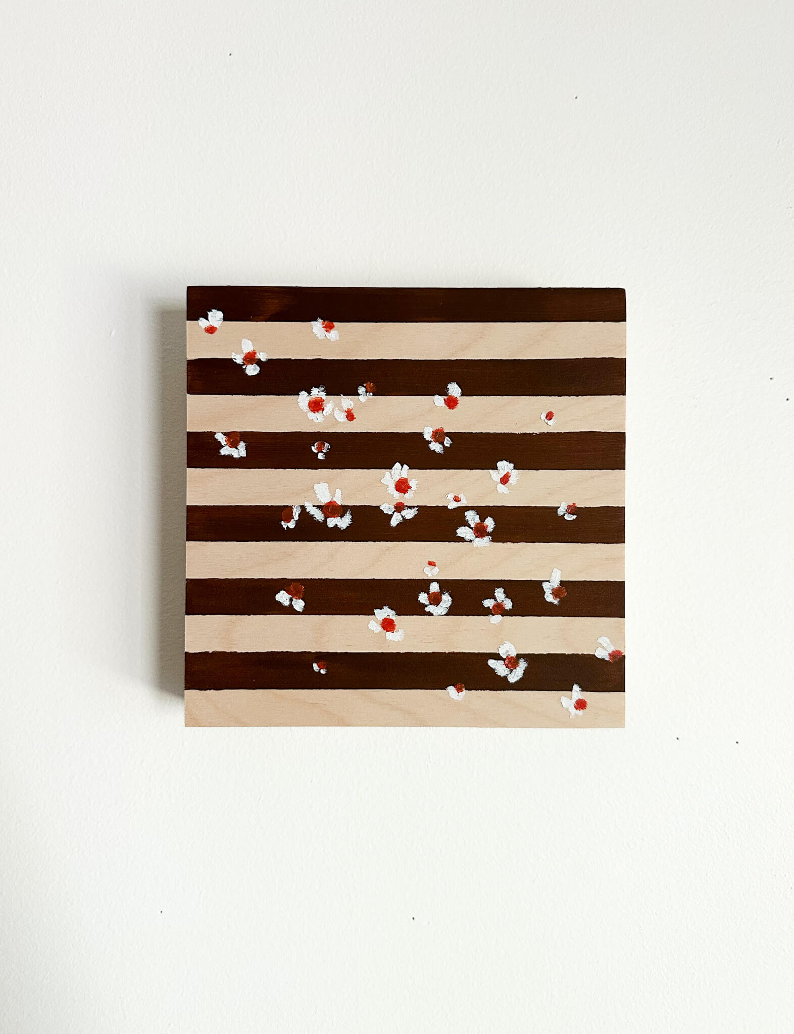 A brown and wood striped background with small white flowers with orange centers scattered across the art.