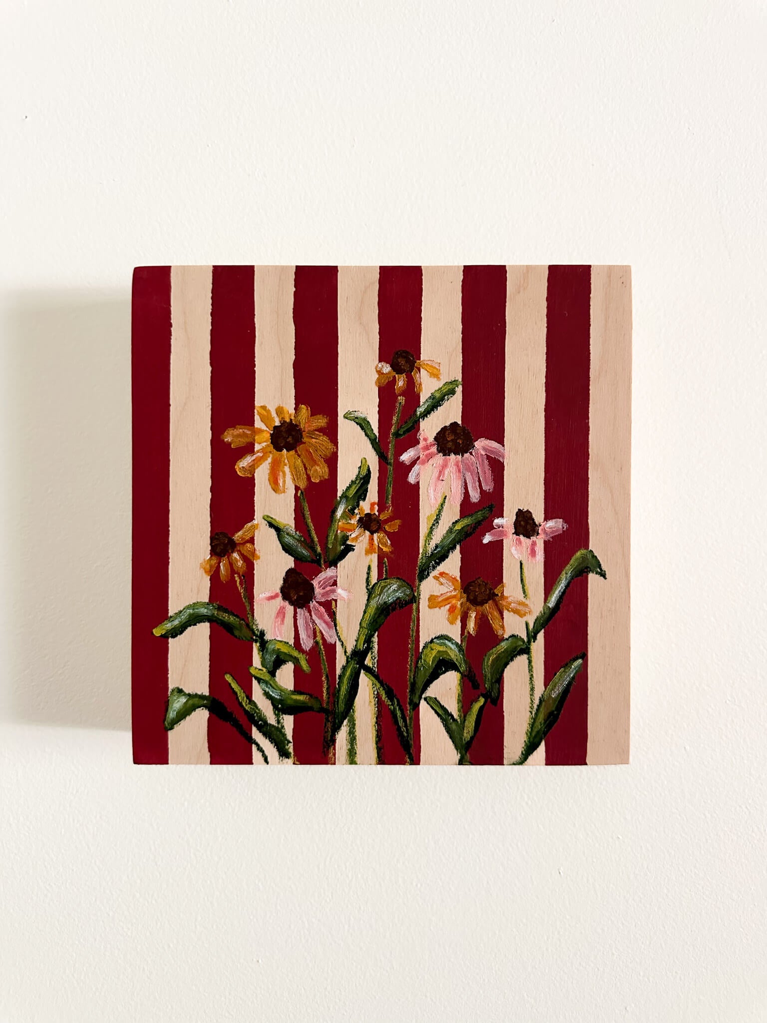 Deep red and wood striped wood panel with oil pastel, pink and yellow cone flowers painted on.