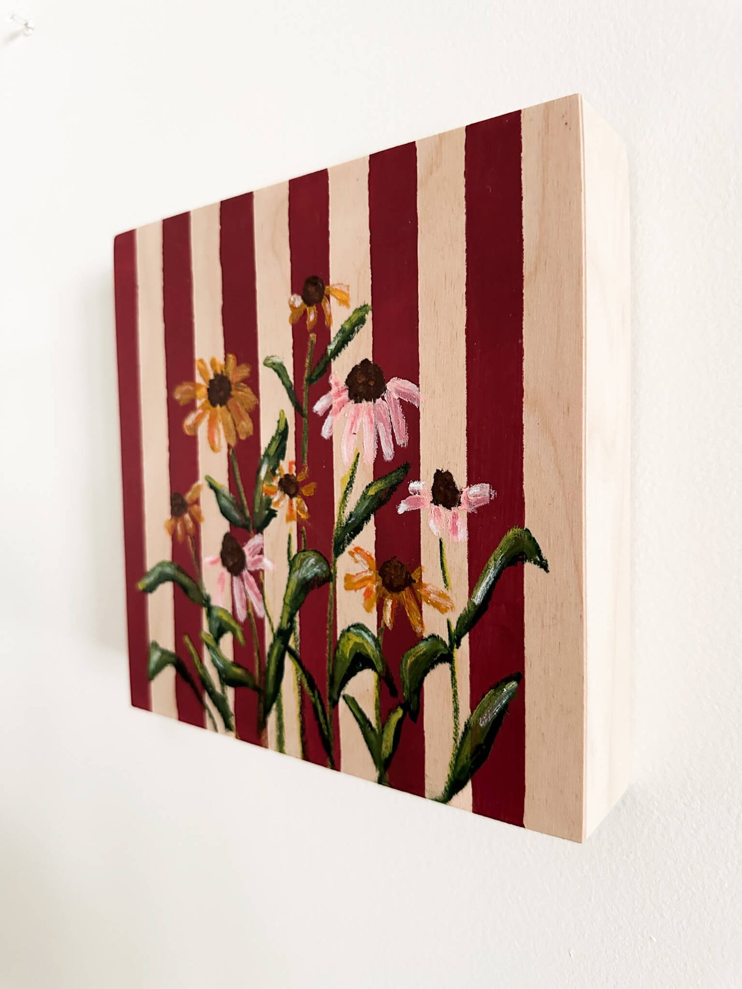 Deep red and wood striped wood panel with oil pastel, pink and yellow cone flowers painted on.