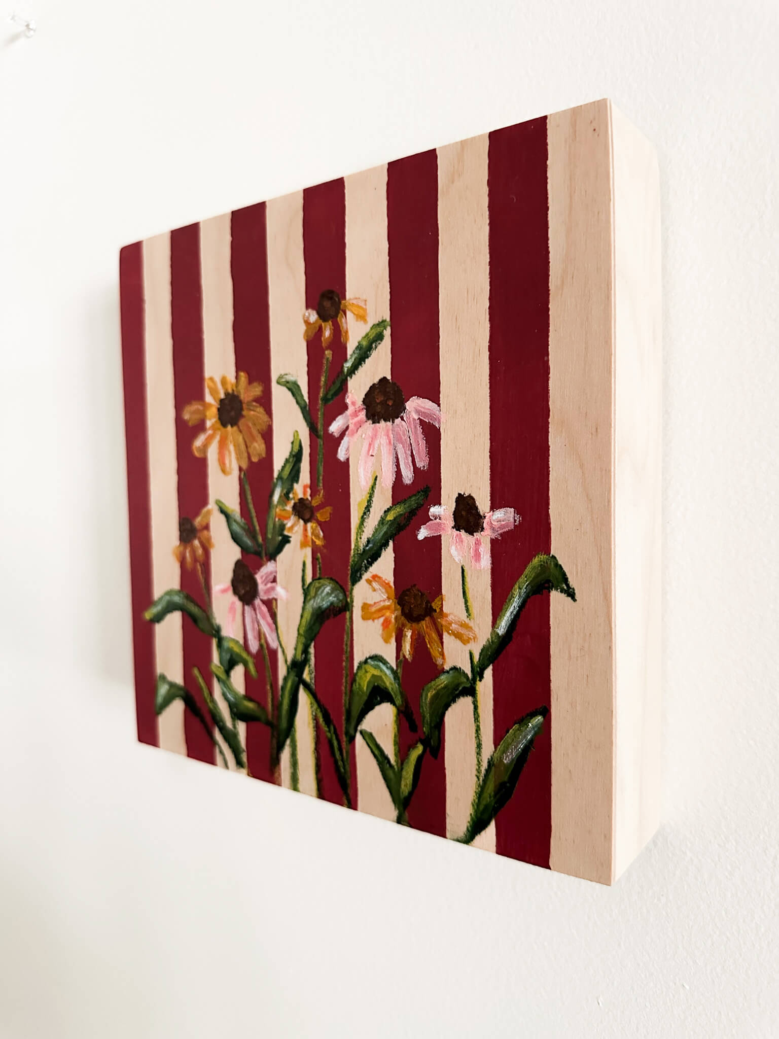 Deep red and wood striped wood panel with oil pastel, pink and yellow cone flowers painted on.