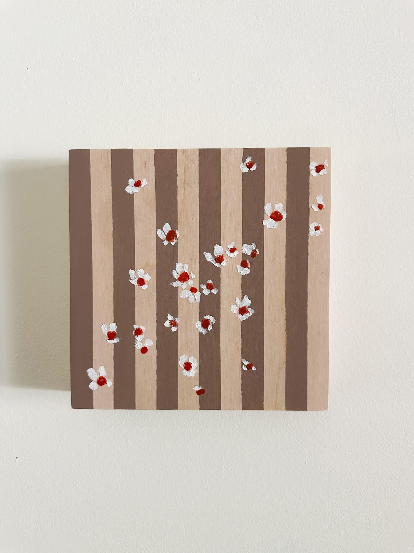 Pattern of white flowers with red centers on brown and wood striped wood panel