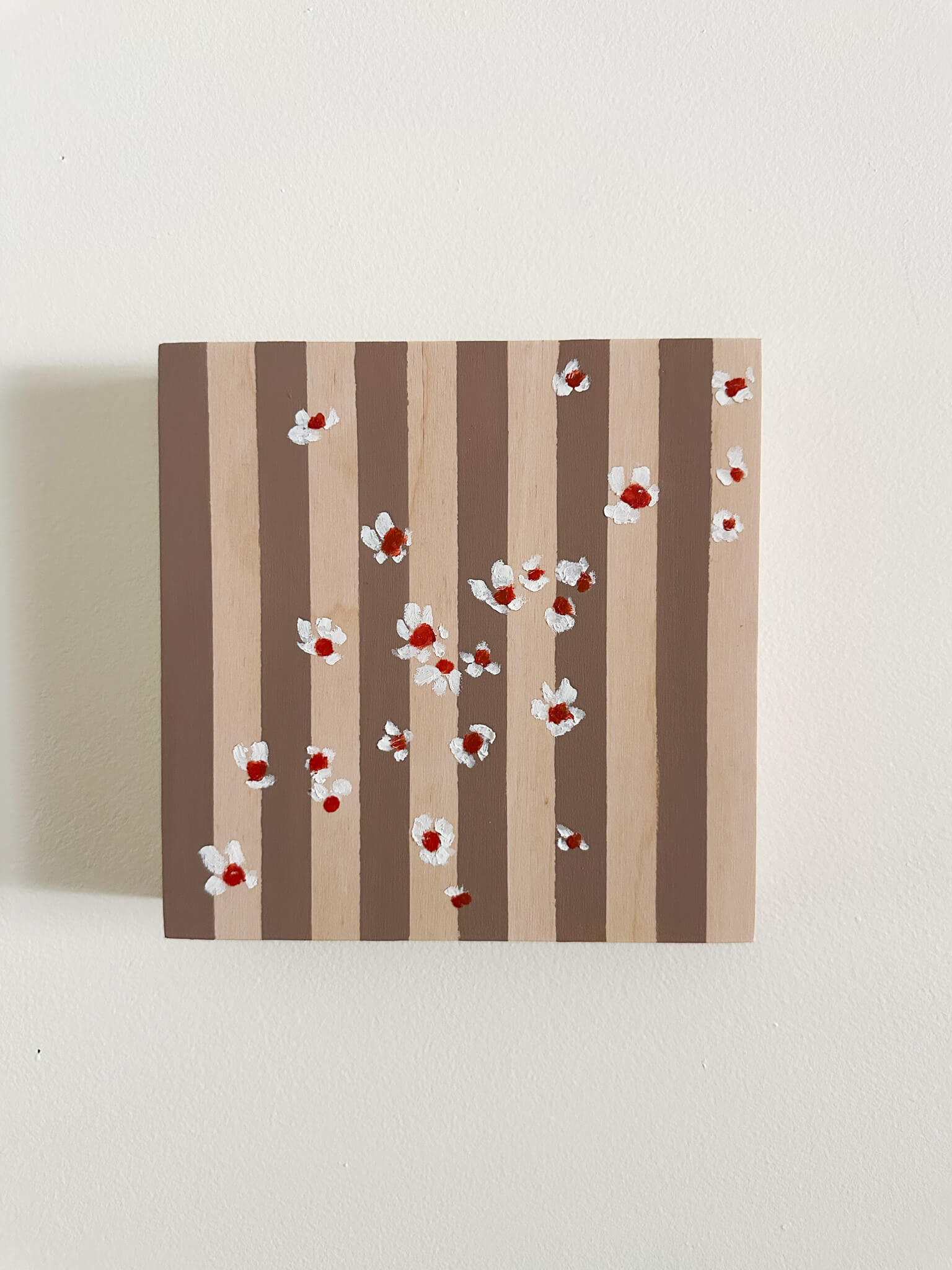 Pattern of white flowers with red centers on brown and wood striped wood panel