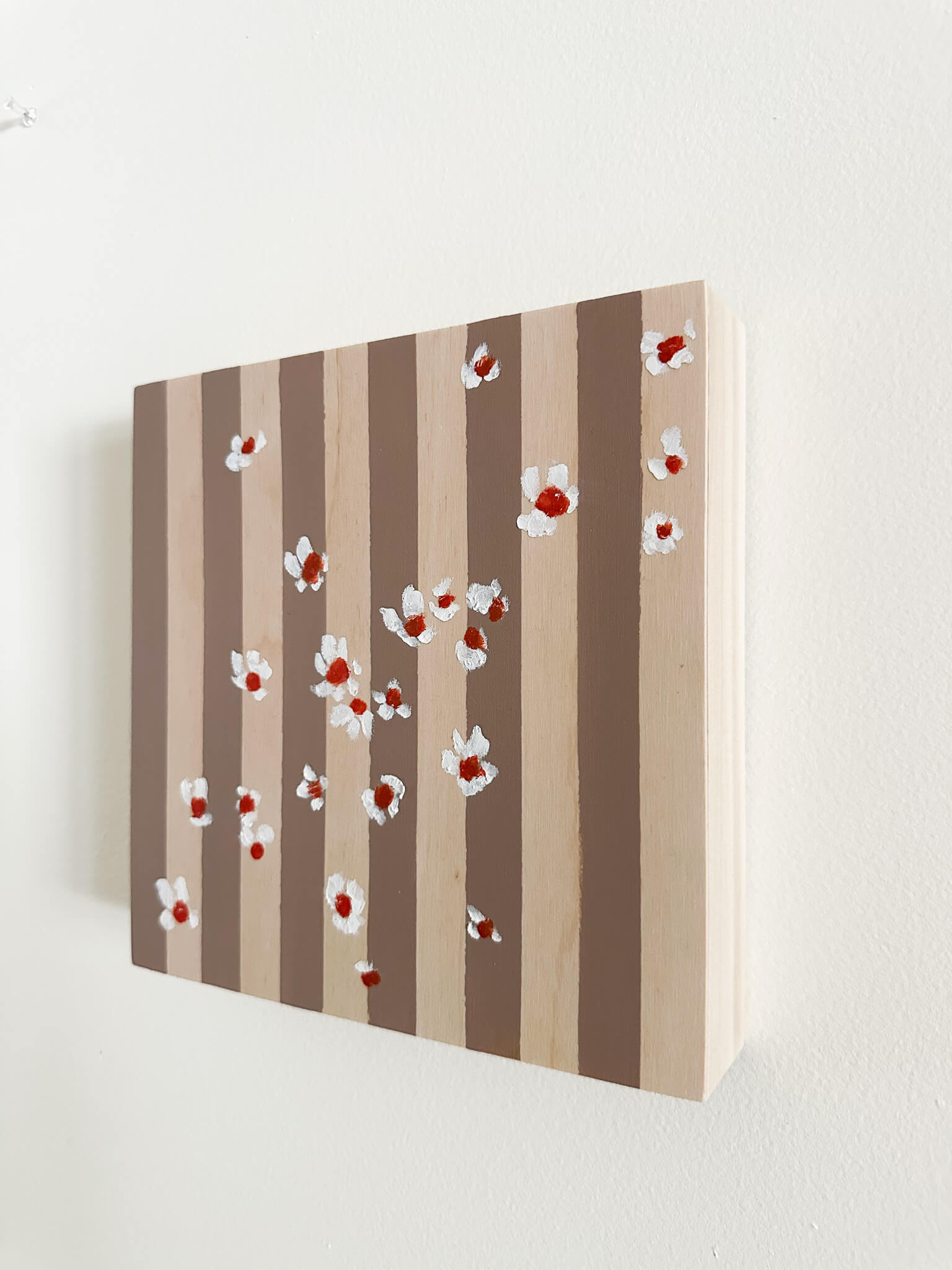 Pattern of white flowers with red centers on brown and wood striped wood panel