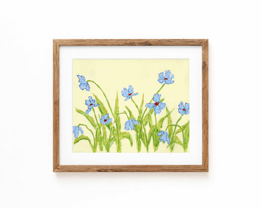 A framed print of blue irises on a pale yellow background, set in a light brown wooden frame with a white mat, displayed against a clean white wall.