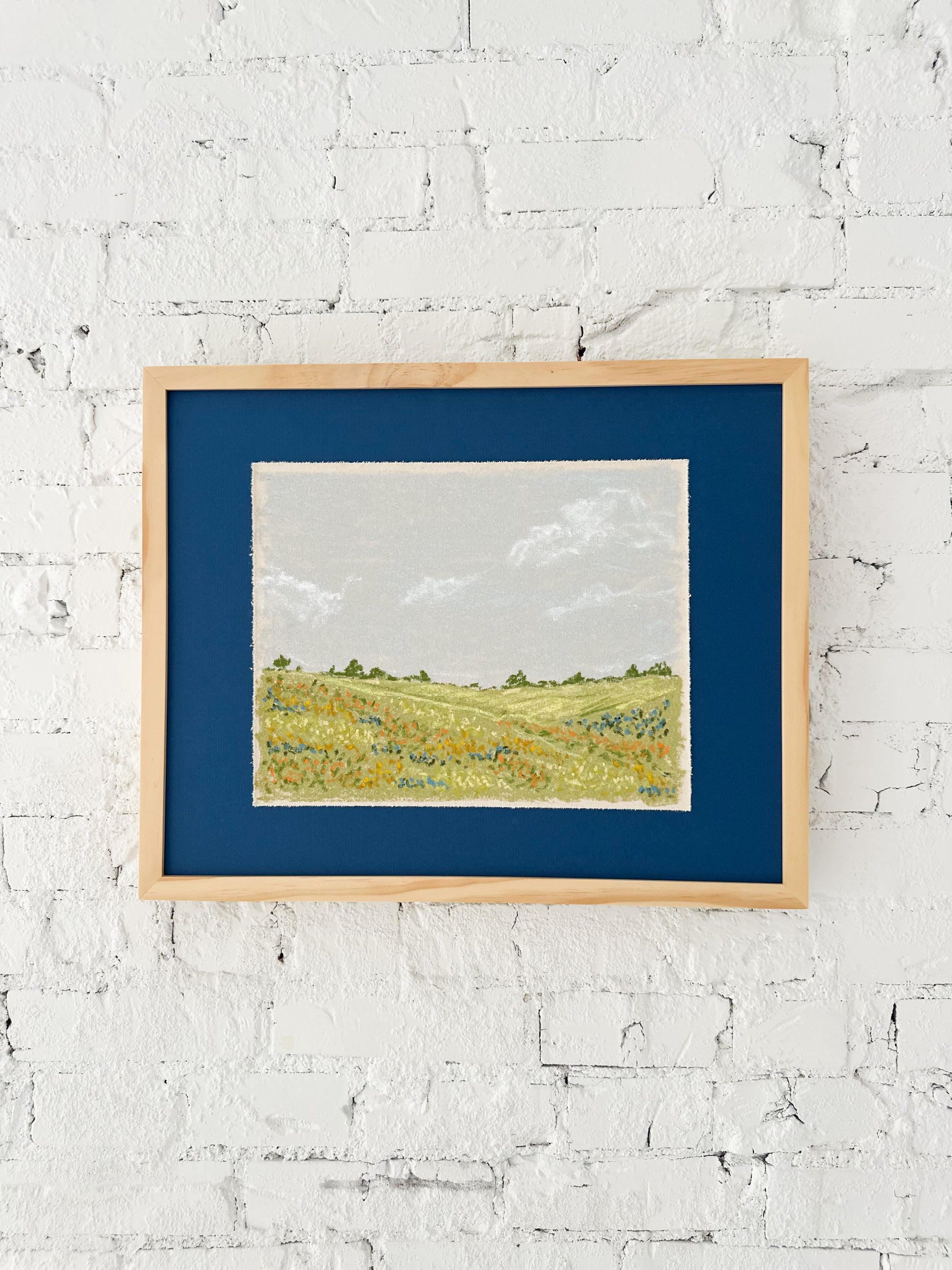 Framed landscape painting on a white brick wall