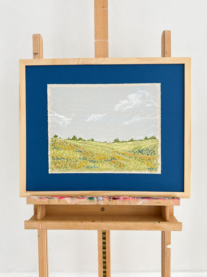 Painting of a landscape on an easel with a blue mat against a white background