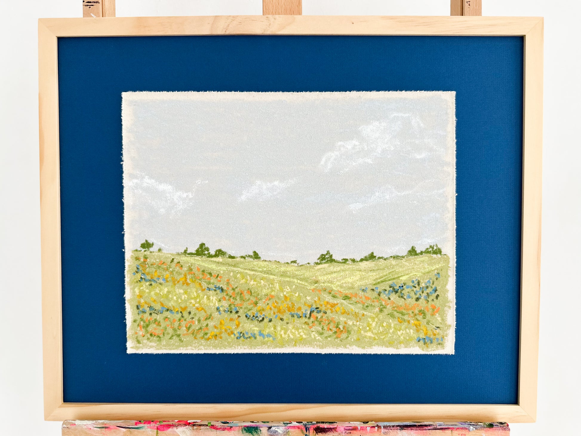 Framed artwork of a landscape with green fields and blue sky.