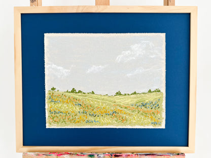 Framed artwork of a landscape with green fields and blue sky.