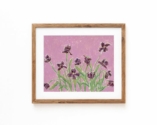 Framed floral wall art featuring purple irises on a textured pink background, set in a light natural wood frame with a white mat against a white wall.
