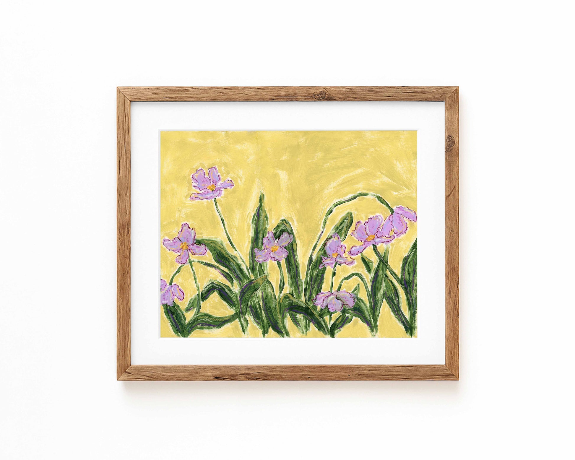 An art print of purple flowers on a green background framed in a natural wood frame and displayed against a white backdrop.