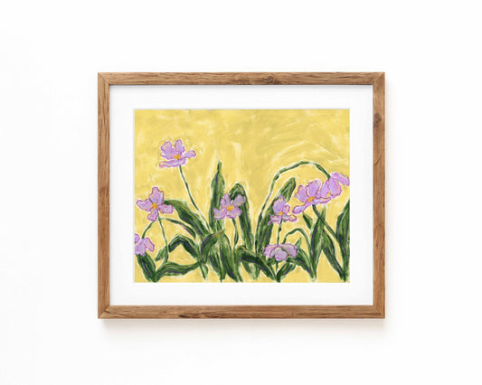 An art print of purple flowers on a green background framed in a natural wood frame and displayed against a white backdrop.