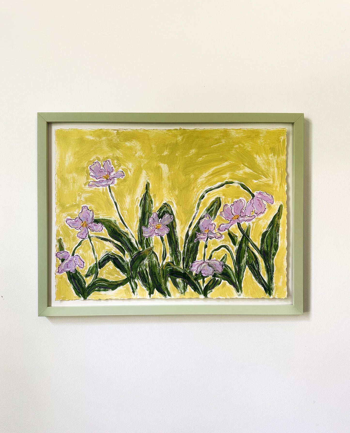 a framed painting of purple flowers on a green background hung on a white wall. 