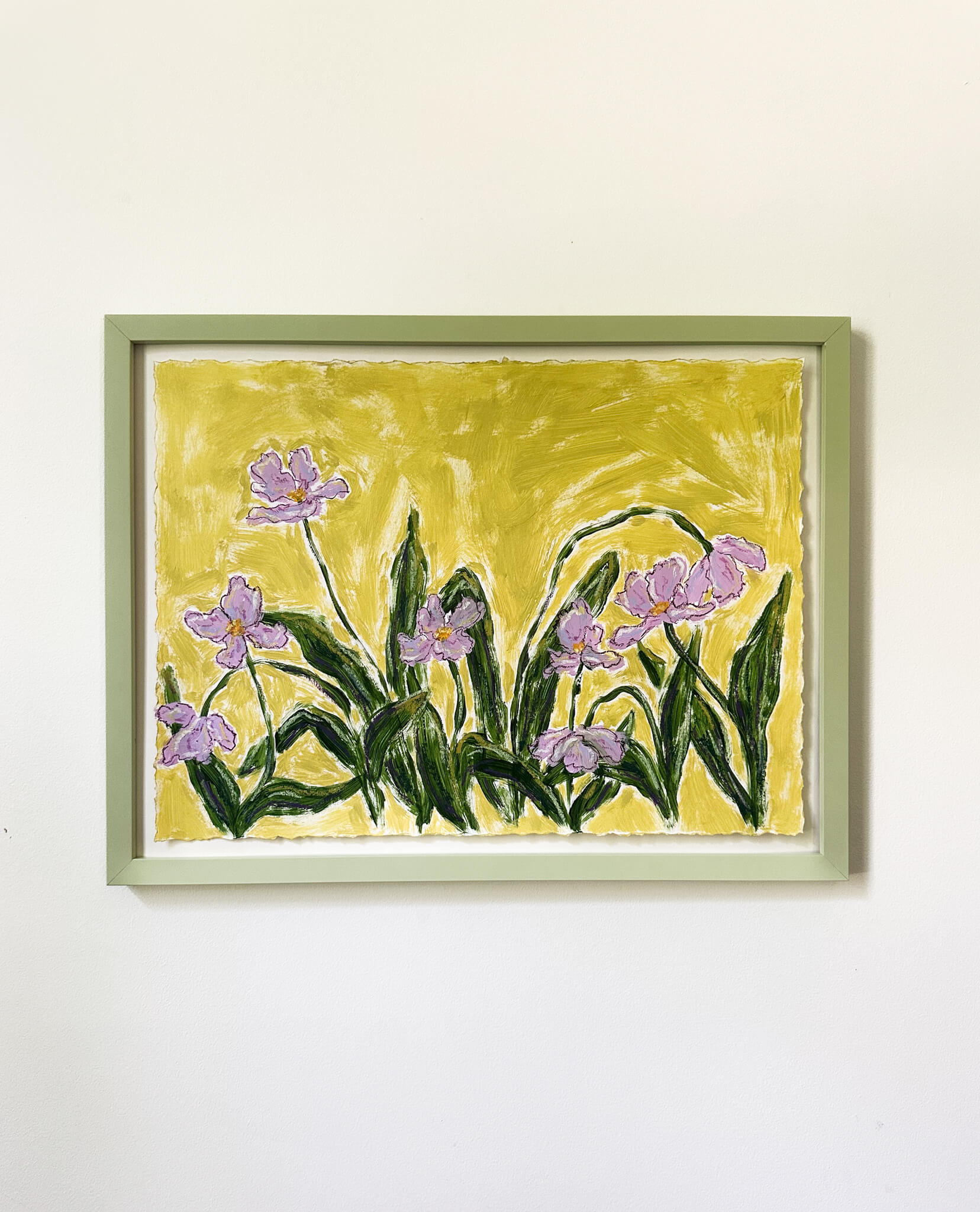 a framed painting of purple flowers on a green background hung on a white wall. 