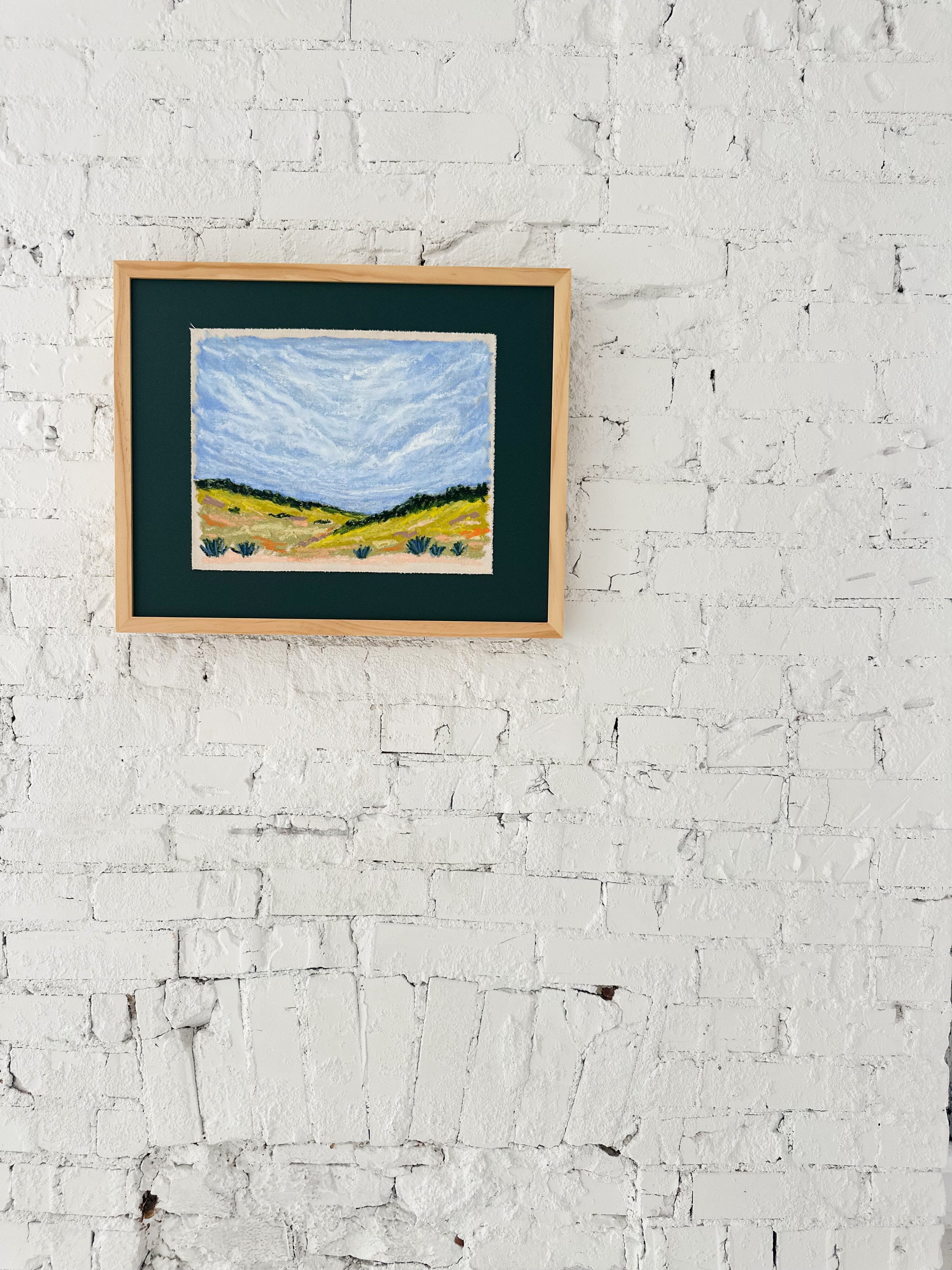 Framed painting of a landscape on a white brick wall