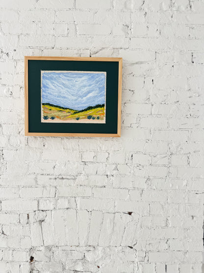 Framed painting of a landscape on a white brick wall