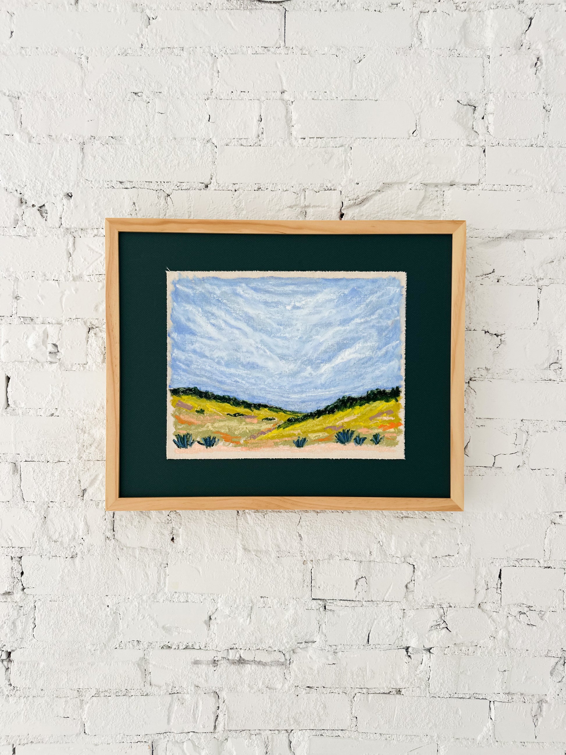 Framed painting of a landscape on a white brick wall