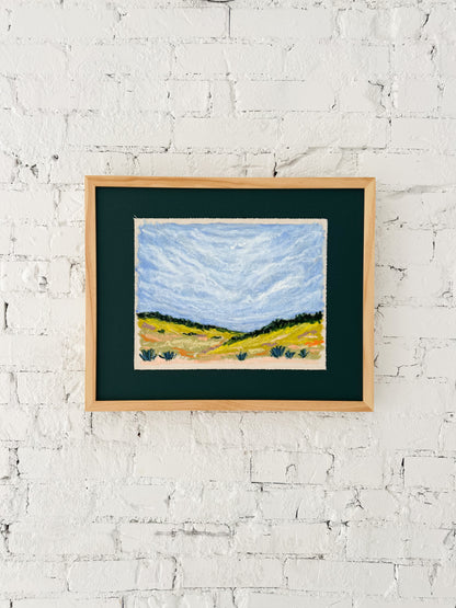 Framed painting of a landscape on a white brick wall