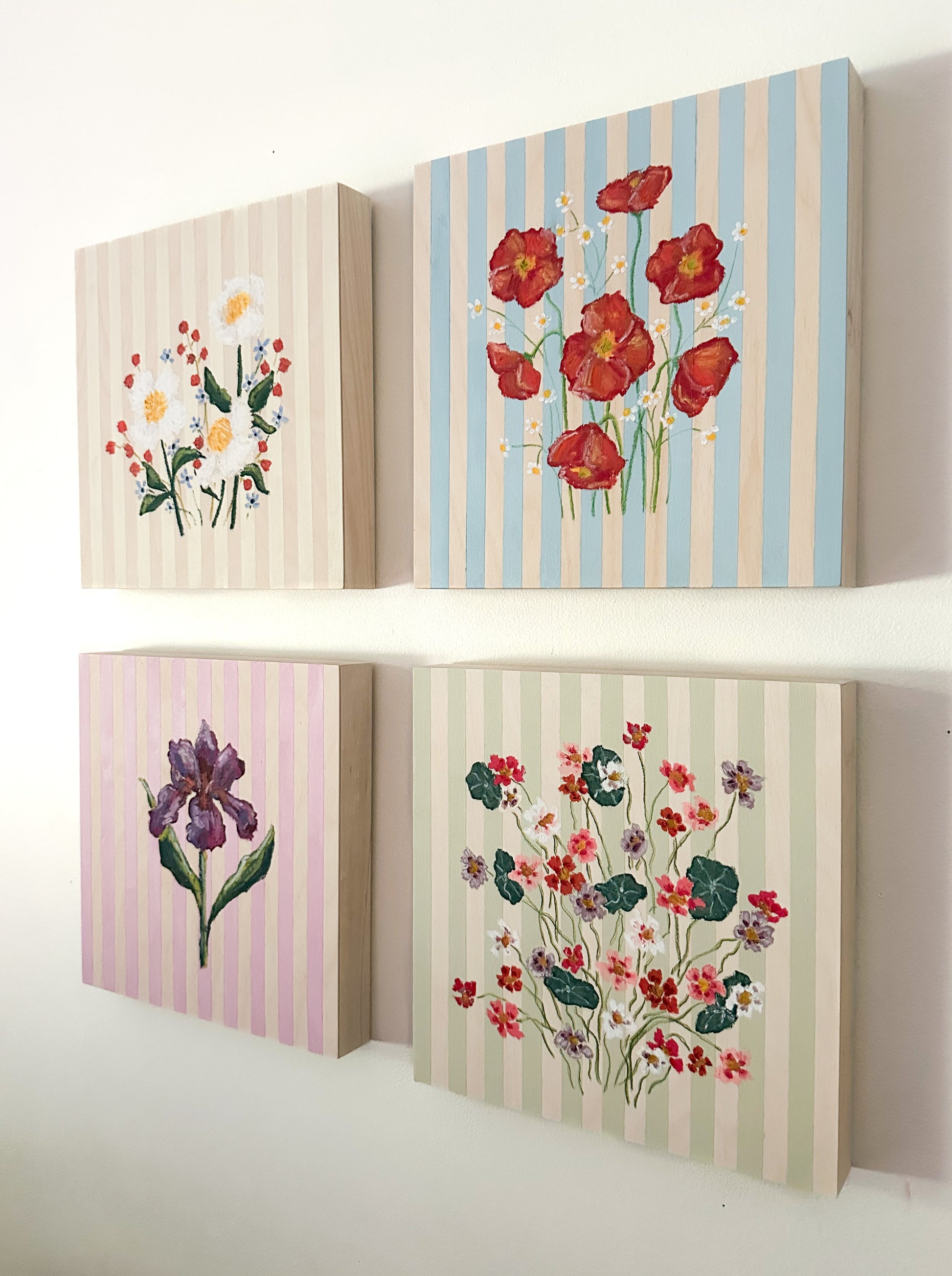 Four floral-themed wall art pieces with striped backgrounds on a white surface.