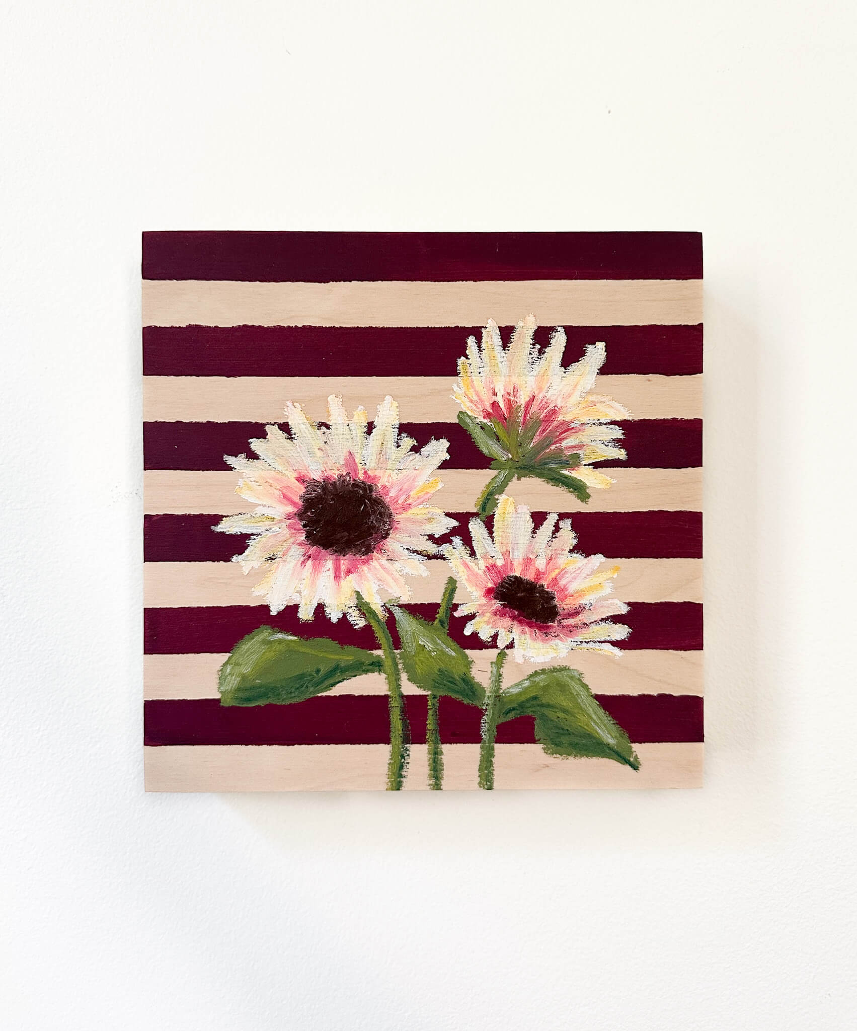 Oil pastel painted sunflowers painted on a red and wood striped, painted wood panel.