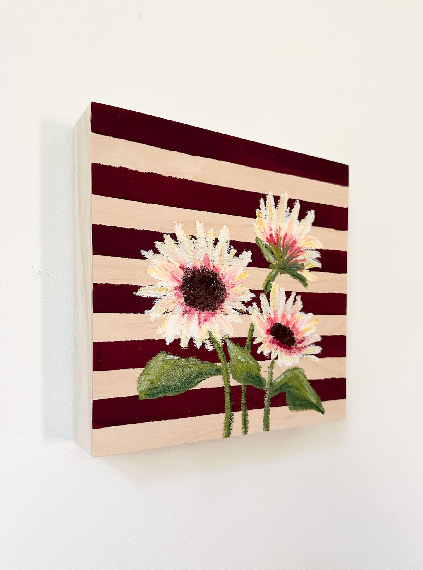 Oil pastel painted sunflowers painted on a red and wood striped, painted wood panel.