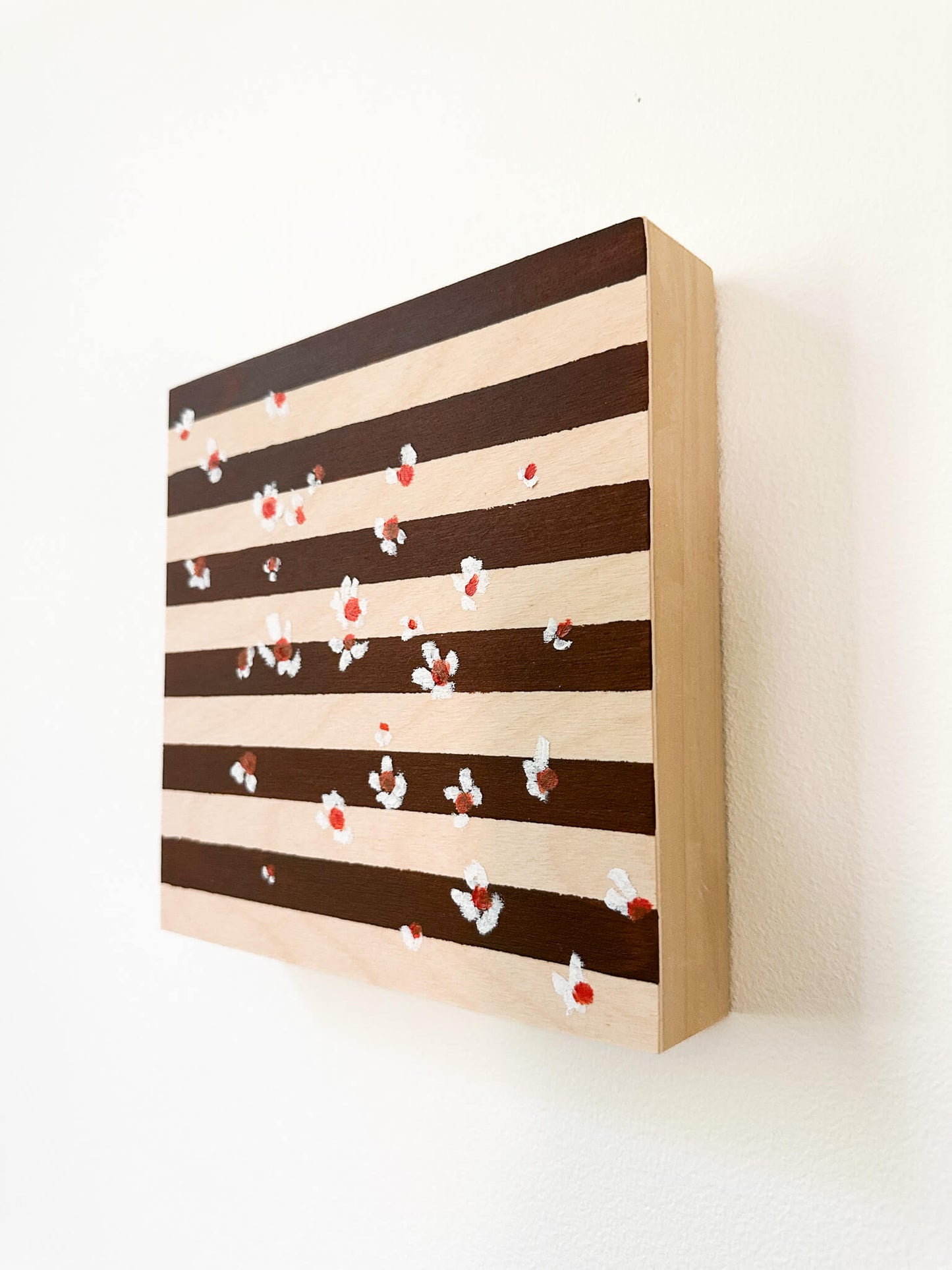 A brown and wood striped background with small white flowers with orange centers scattered across the art. 