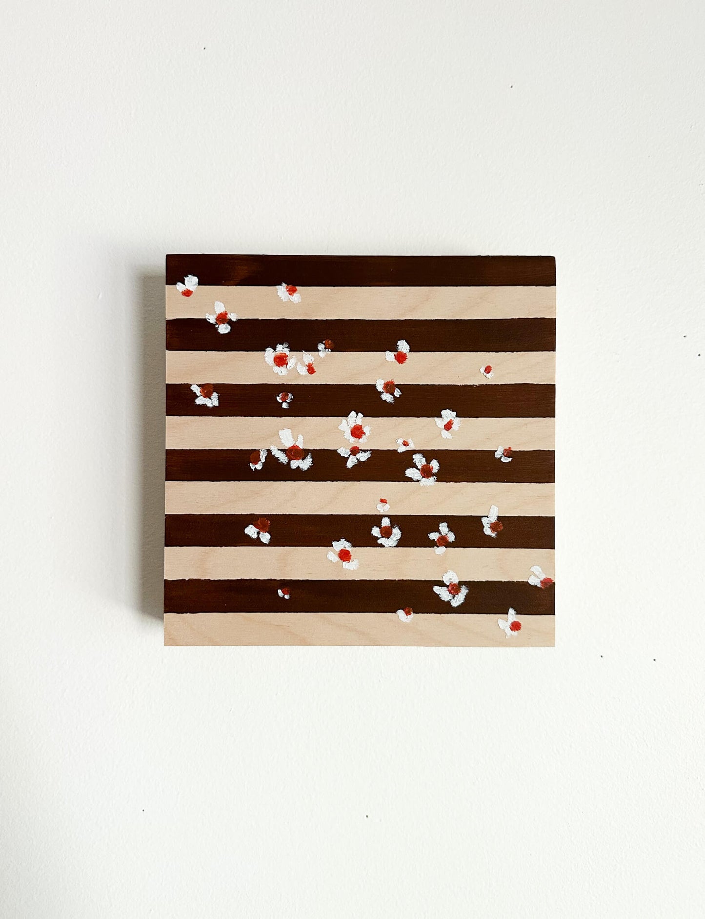 A brown and wood striped background with small white flowers with orange centers scattered across the art. 