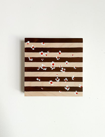 A brown and wood striped background with small white flowers with orange centers scattered across the art. 