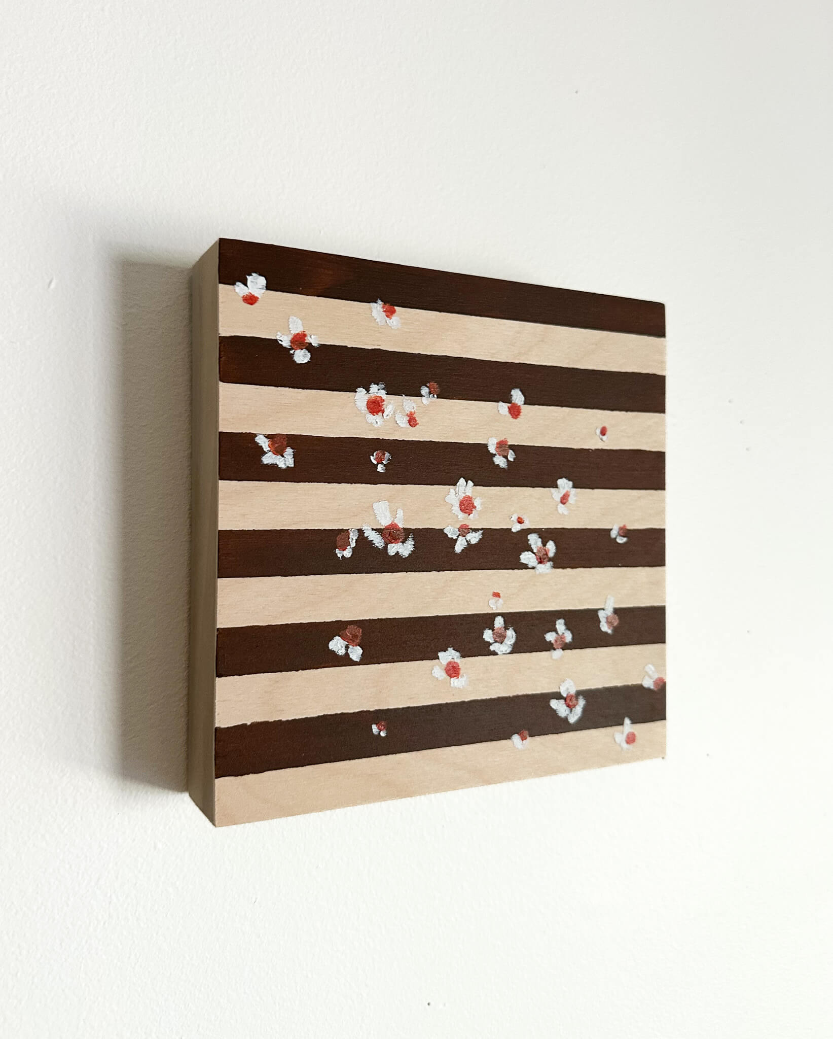A brown and wood striped background with small white flowers with orange centers scattered across the art. 