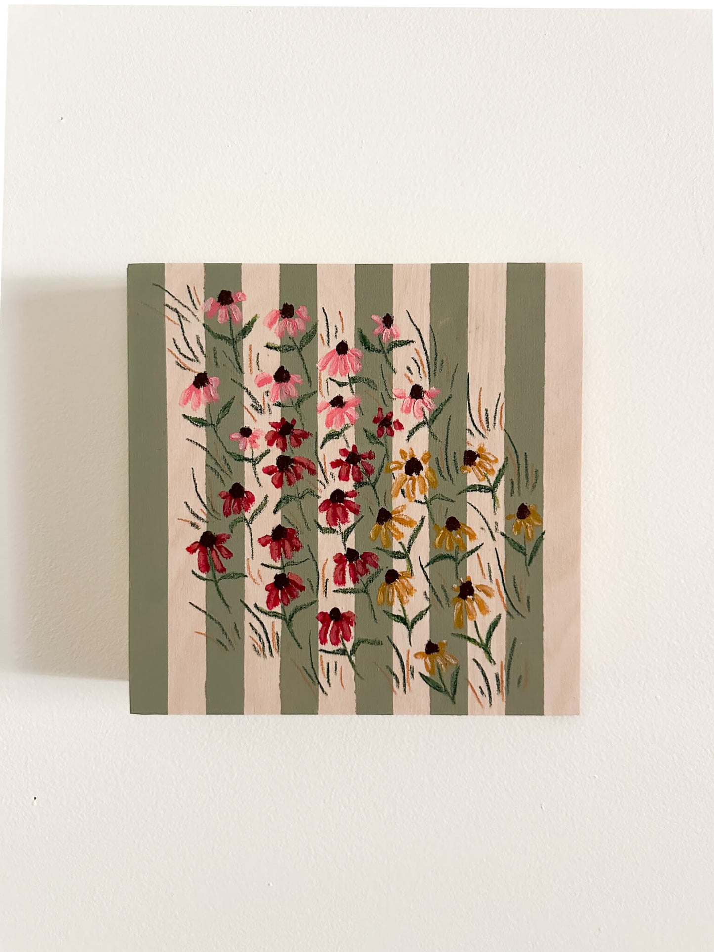 small pink, red, and yellow coneflowers on a green and wood striped wood panel.