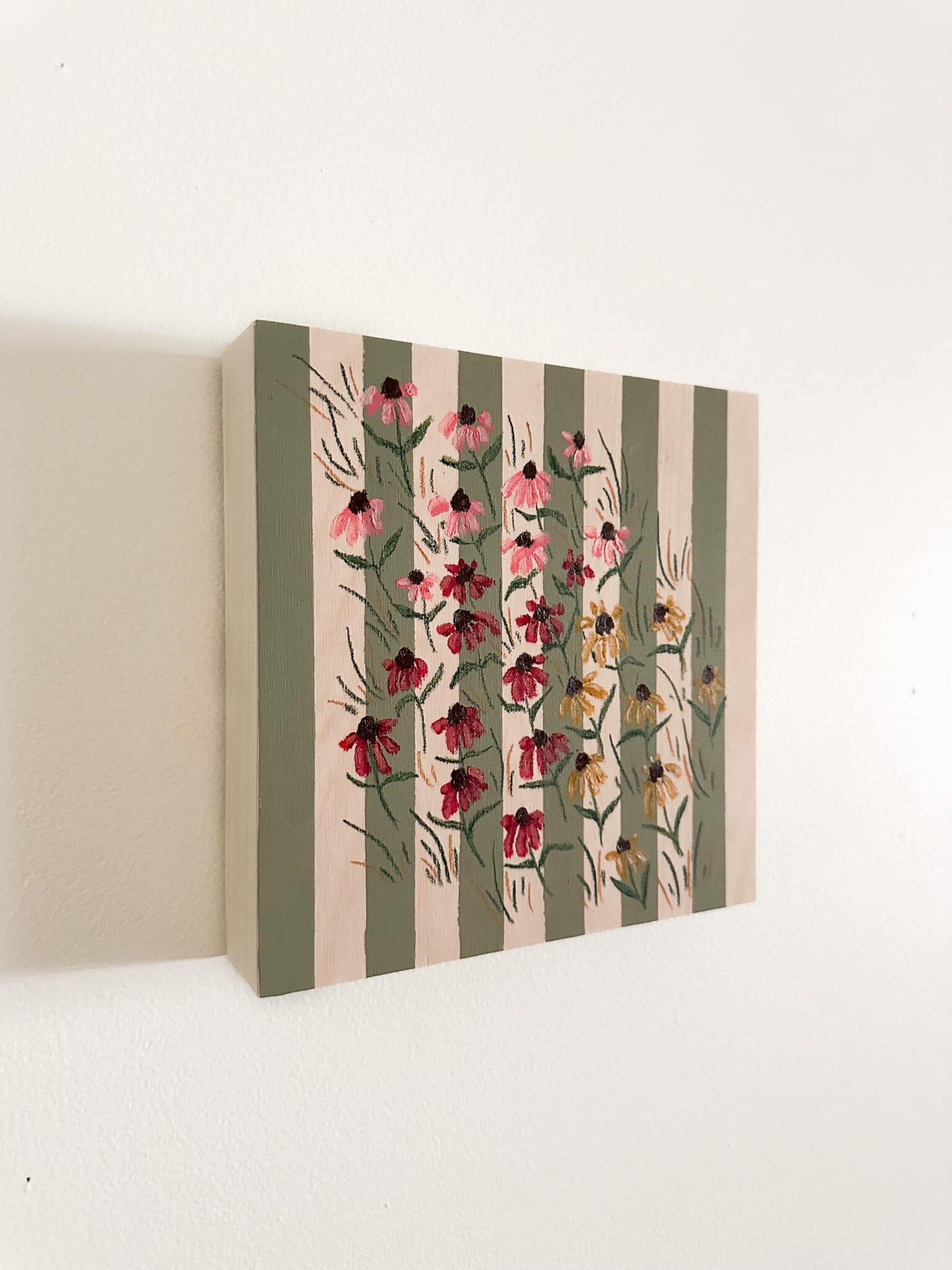 small pink, red, and yellow coneflowers on a green and wood striped wood panel.