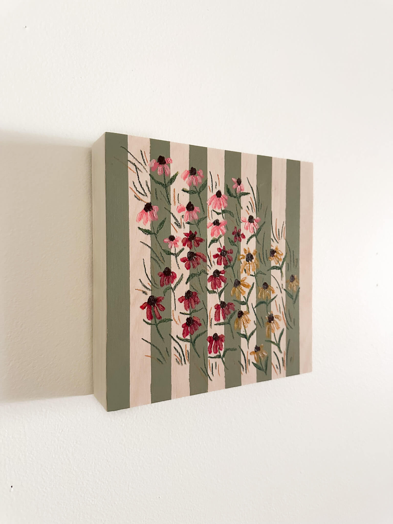 small pink, red, and yellow coneflowers on a green and wood striped wood panel.