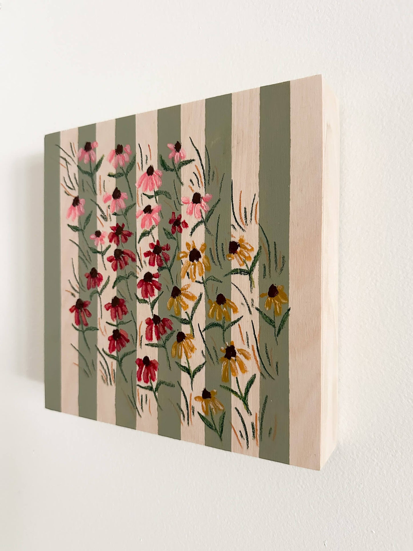 small pink, red, and yellow coneflowers on a green and wood striped wood panel.