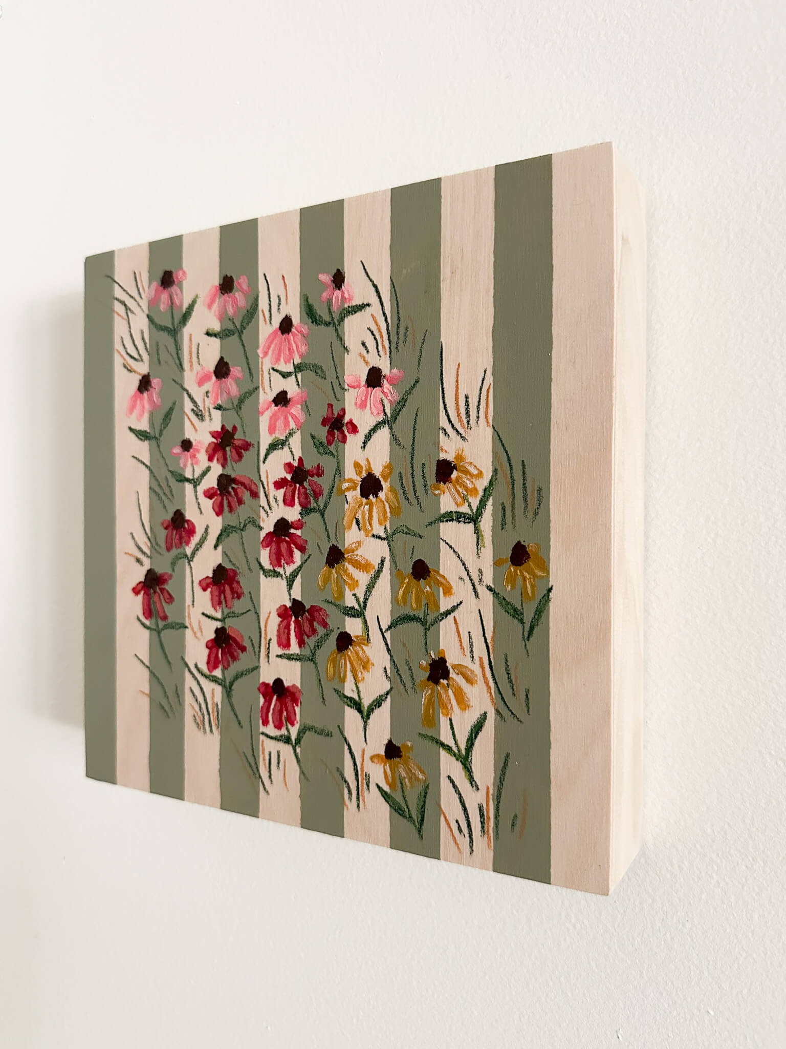 small pink, red, and yellow coneflowers on a green and wood striped wood panel.