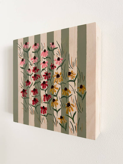small pink, red, and yellow coneflowers on a green and wood striped wood panel.