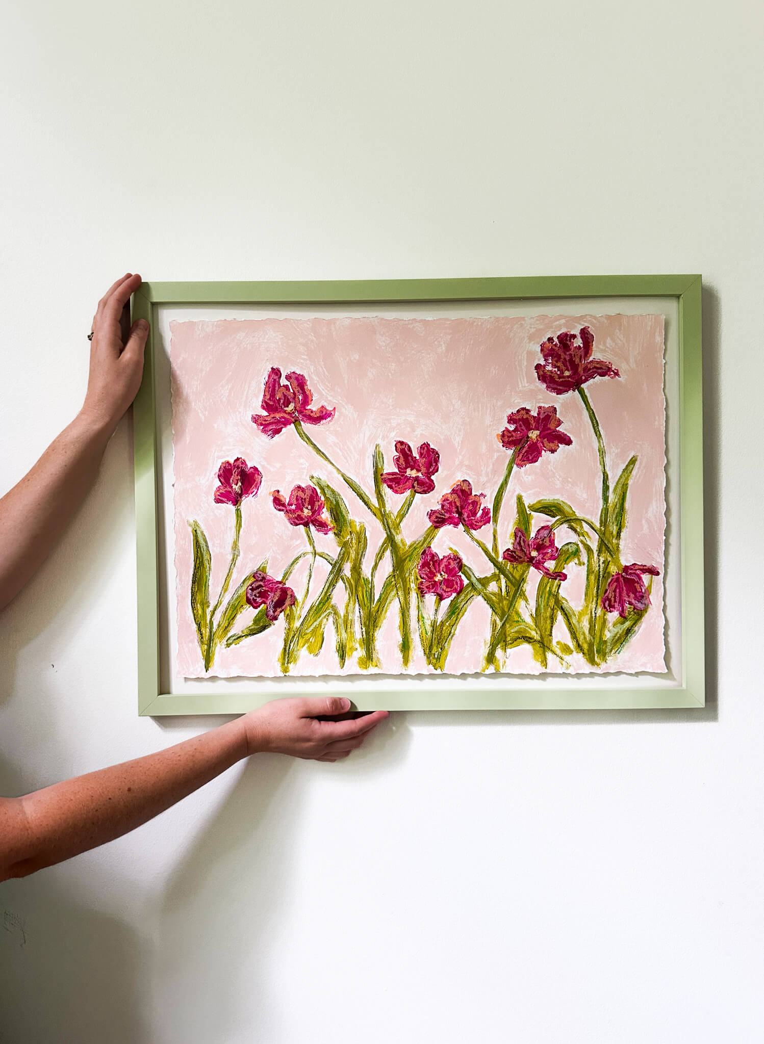 Person holding a framed artwork of pink flowers on a white wall