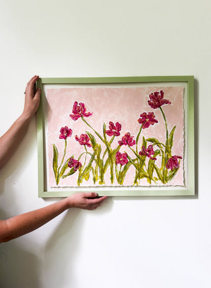 Person holding a framed artwork of pink flowers on a white wall