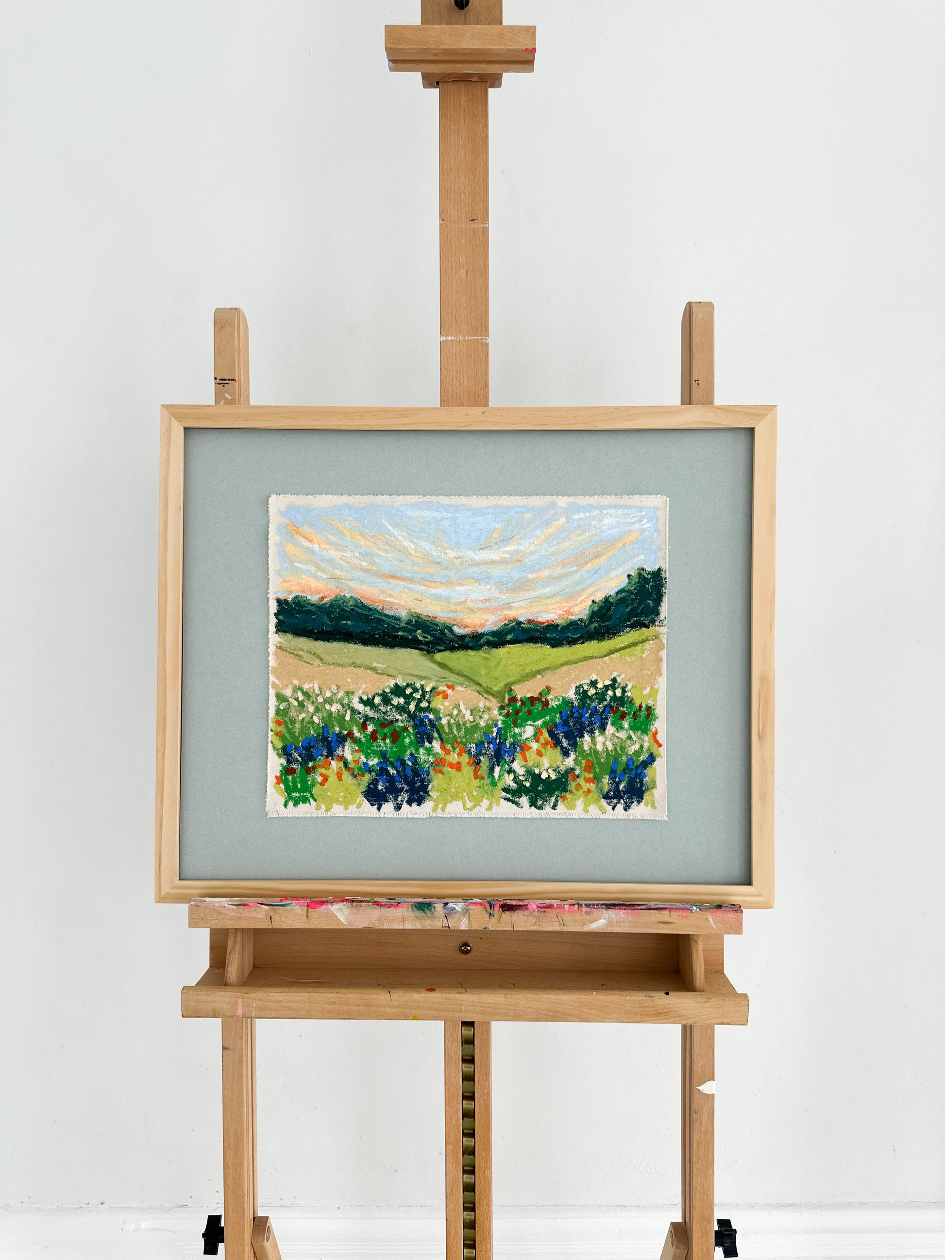 Painting of a landscape with flowers on an easel against a white background