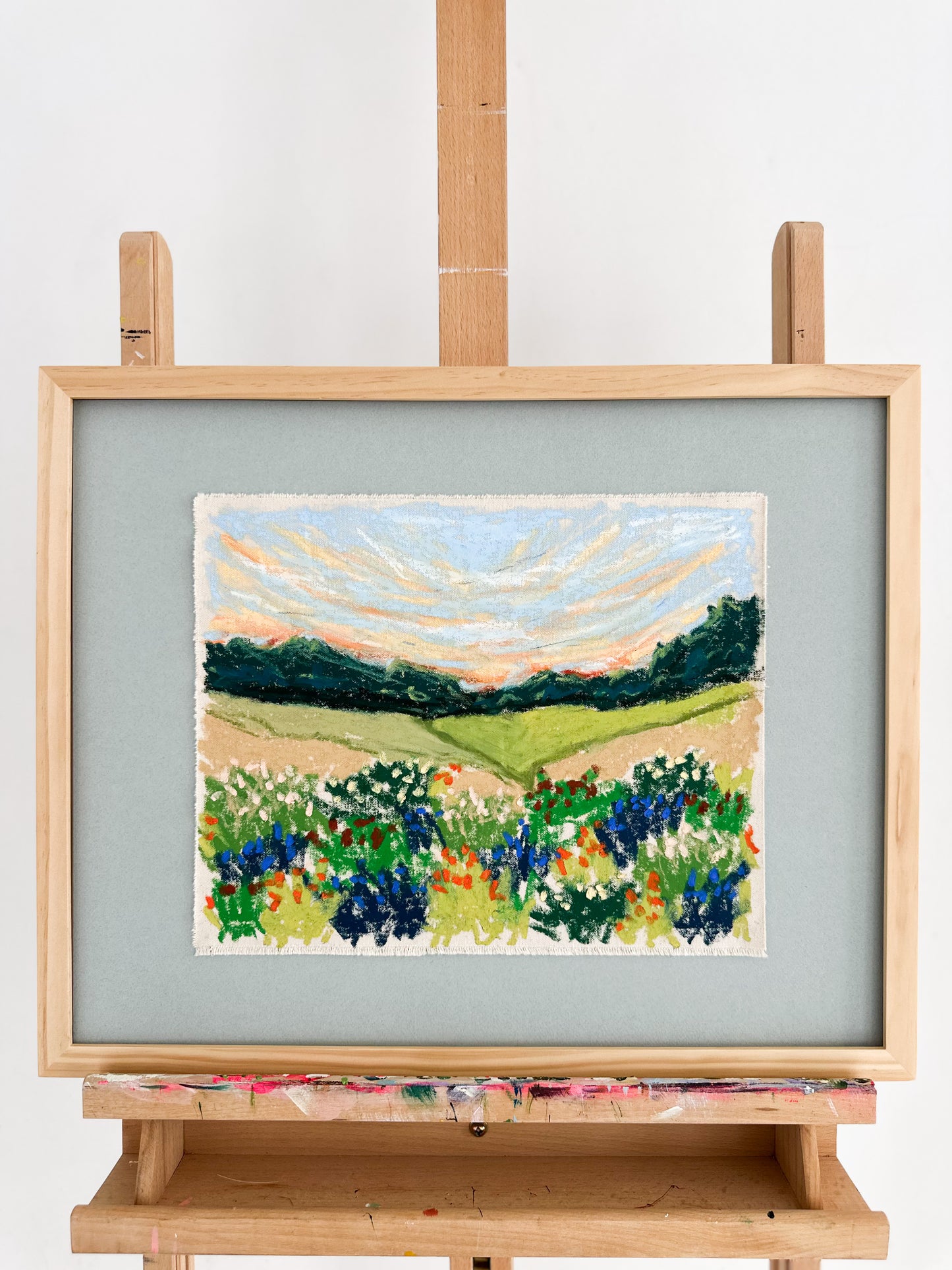 Framed painting of a landscape with fields and trees on an easel.