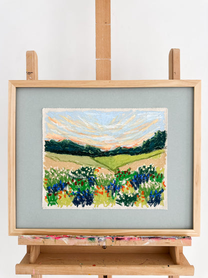 Framed painting of a landscape with fields and trees on an easel.