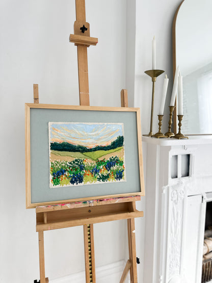 Painting of a landscape with flowers on an easel against a white wall.