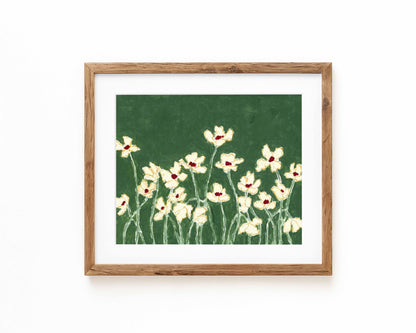 An art print of white flowers on a green background framed in a natural wood frame and displayed against a white backdrop.