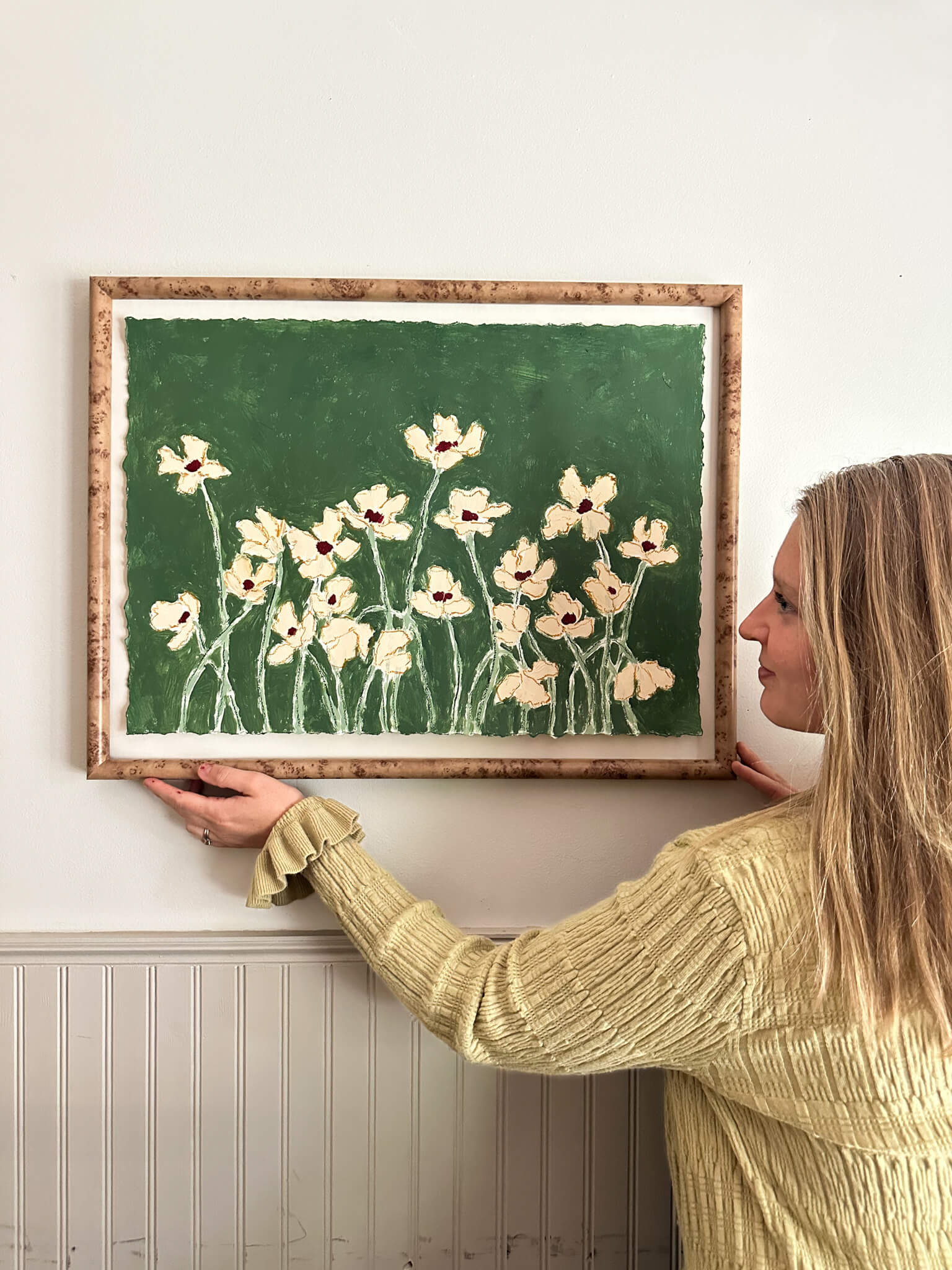 Woman hanging a framed artwork of flowers on a wall