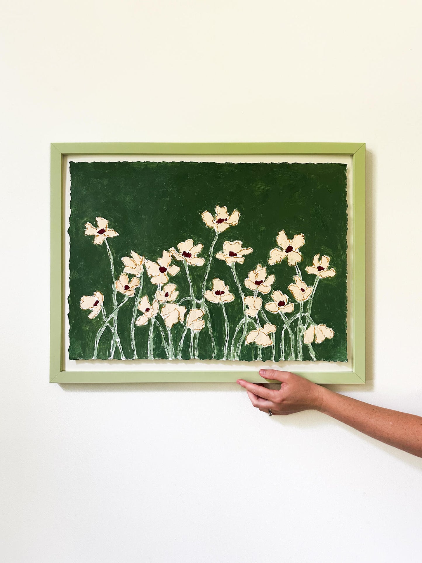 Framed artwork of flowers on a green background held by a hand