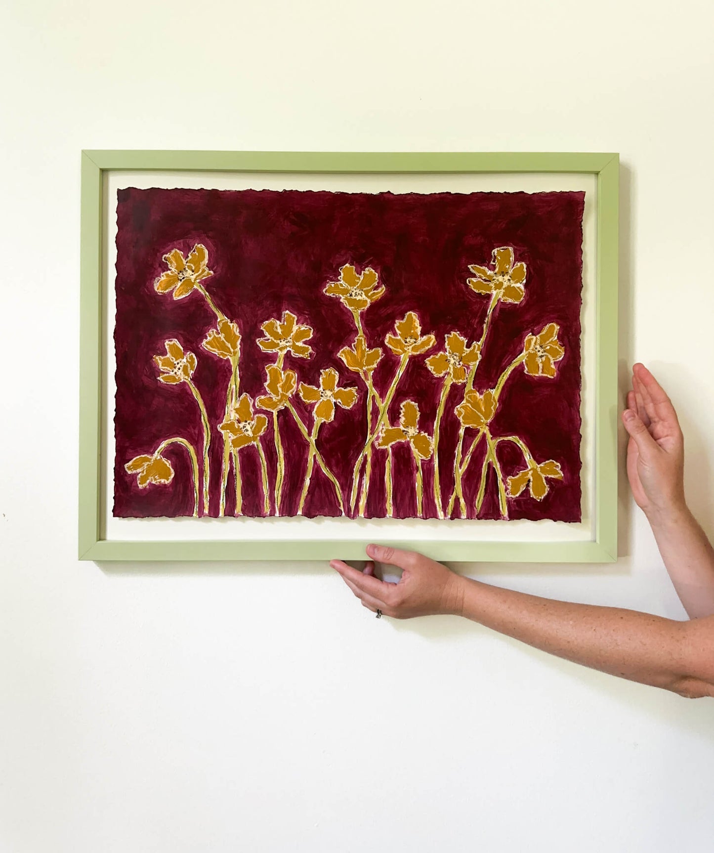 Framed artwork with floral design on a red background, held by a person.