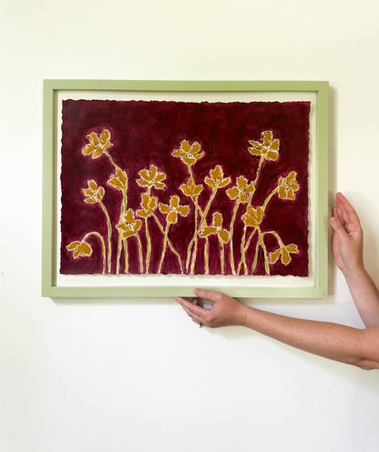 Framed artwork with floral design on a red background, held by a person.