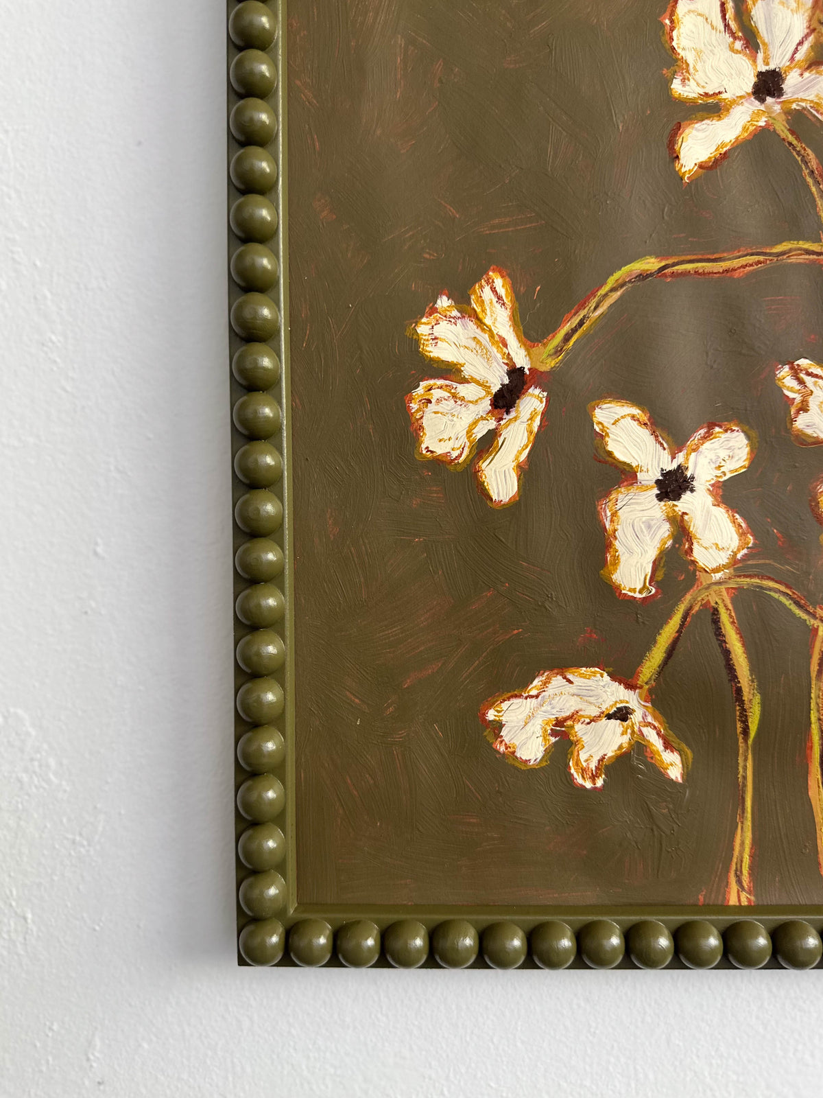 The corner of a painting of off white flowers with green stems  on a  thyme green background framed in a thyme green bobbin frame.