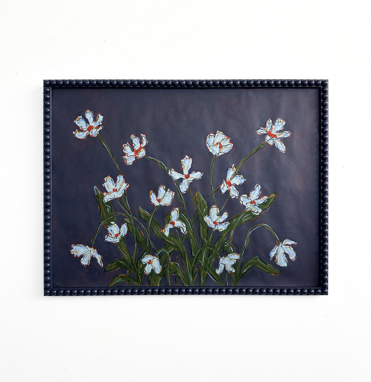 A painting of light blue flowers with green leaves on a dark blue background framed in a dark blue bobbin frame and hanging on a white wall. 