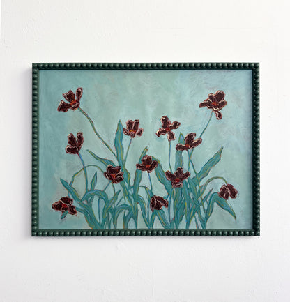 A painting of light pink flowers with green stems on a pink background and framed in a light pink bobbin frame. The painting is hung on a white wall.