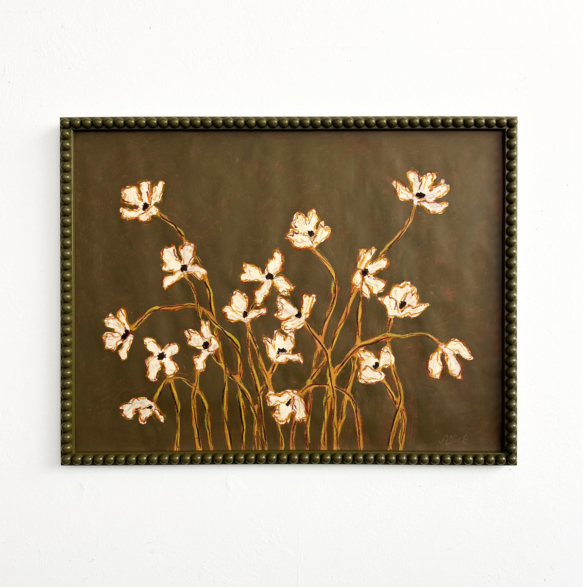 A painting of off white flowers with green stems  on a  thyme green background framed in a thyme green bobbin frame hanging on a white wall.
