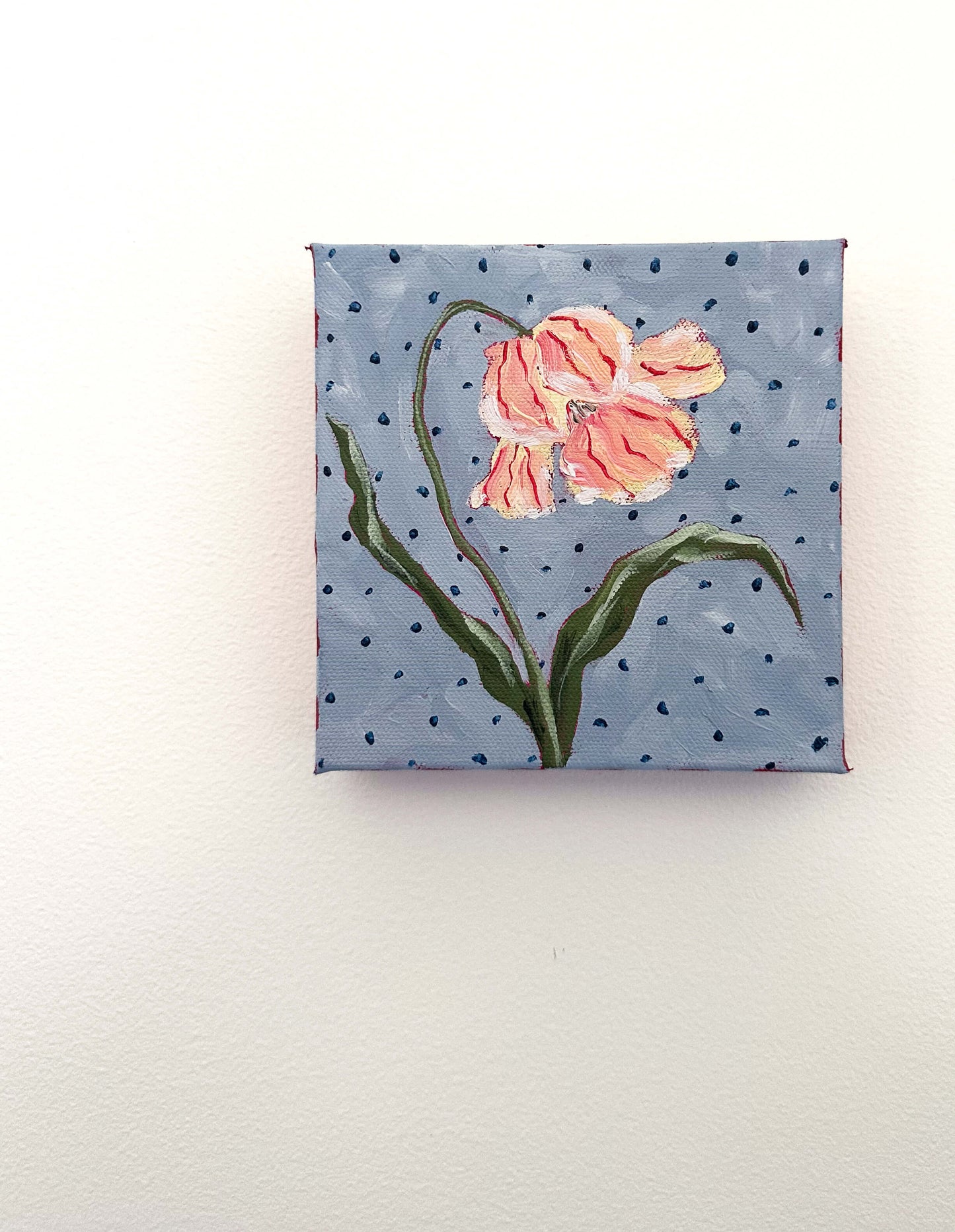 Small painting of a pink flower on a blue polka dot background
